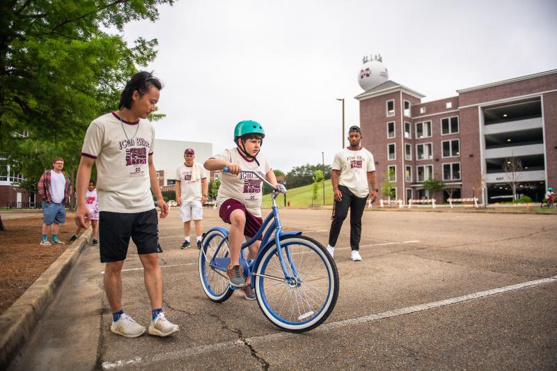 MSU students teaching a child to ride a bike